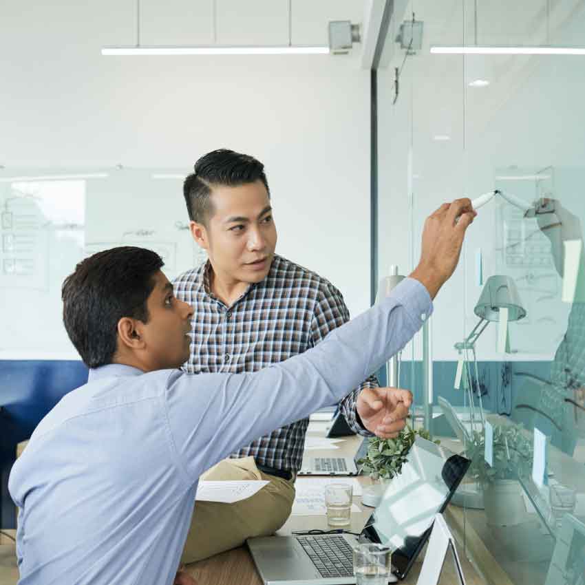 Photo de deux hommes travaillant sur un tableau blanc
